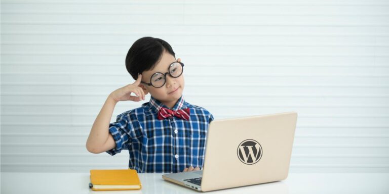 Nuori poika, jolla on silmälasit ja rusetti, käyttää kannettavaa tietokonetta, jossa on WordPress-logo.